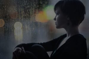 sad girl on the windowsill looking out the window